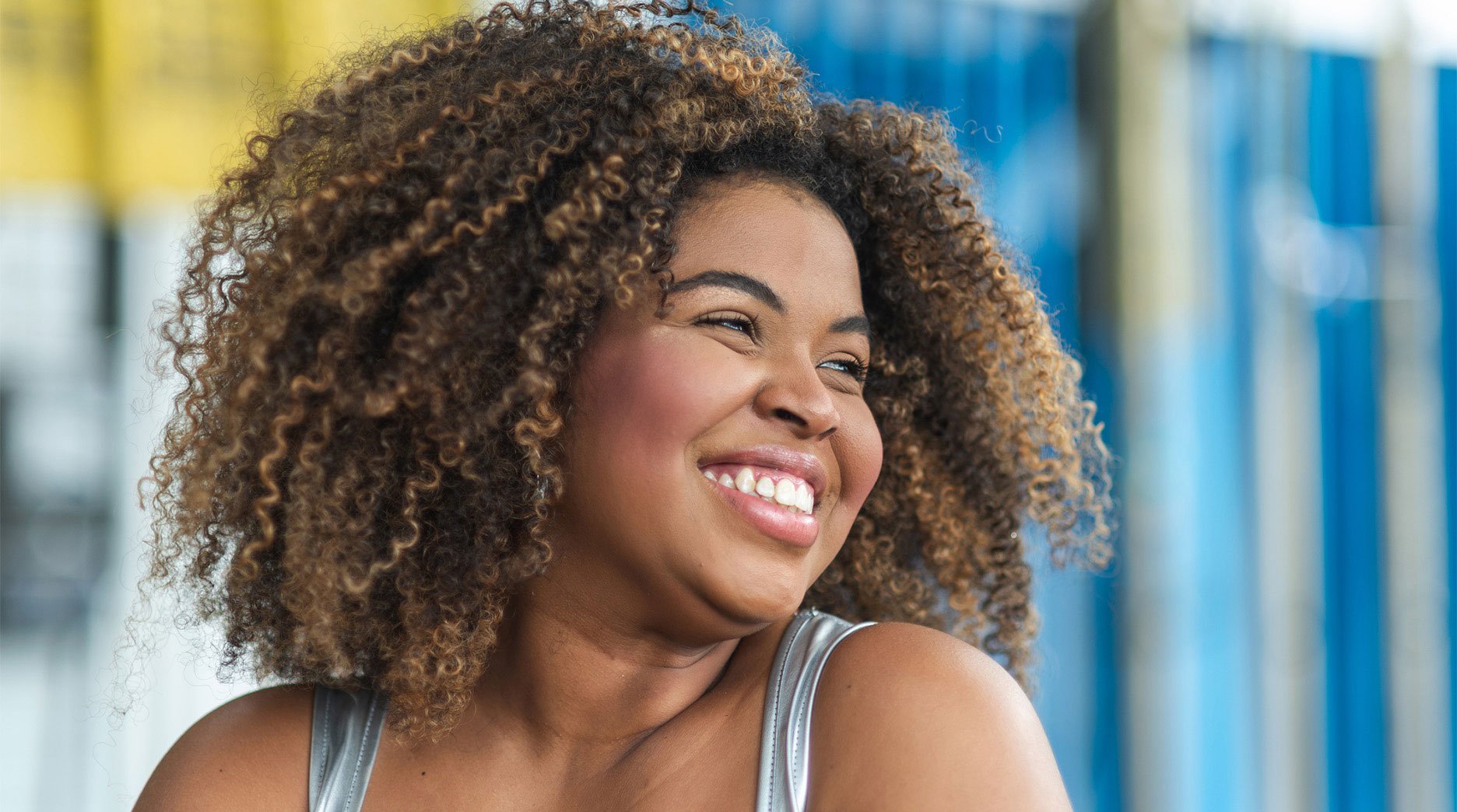 Portrait of young woman with 4A curls looking to the side, smiling.